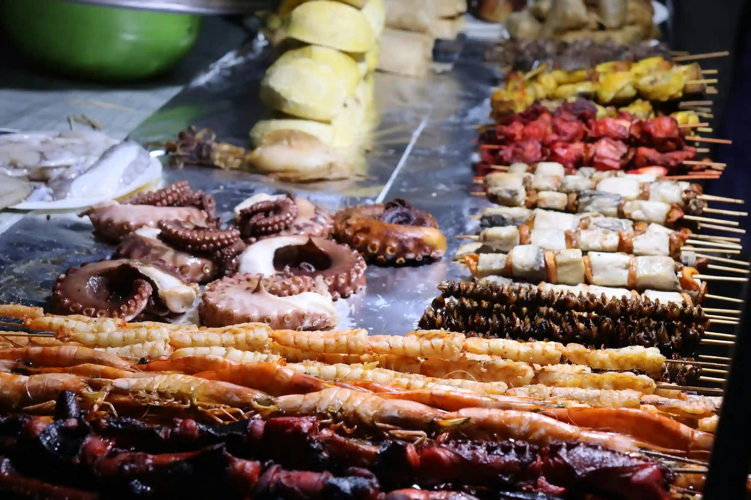 A close-up of fresh seafood, including grilled octopus, shrimp, and skewers, displayed at a food stall in the Forodhani night market in Zanzibar.