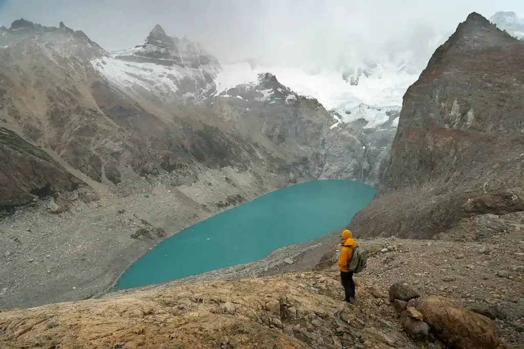 Hiker overlooking the turquoise Laguna de los Tres and snow-covered peaks near El Chaltén in Argentine Patagonia.