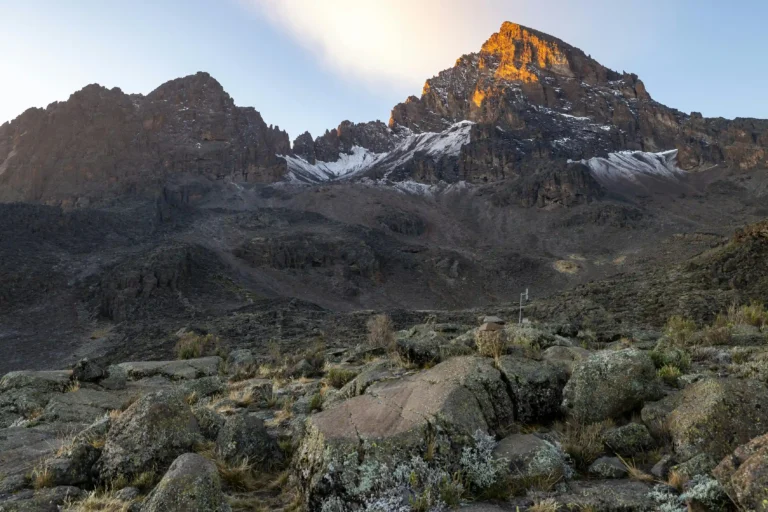 The first light of day on Batian Peak, the highest point of Mount Kenya, with a rugged, rocky landscape below