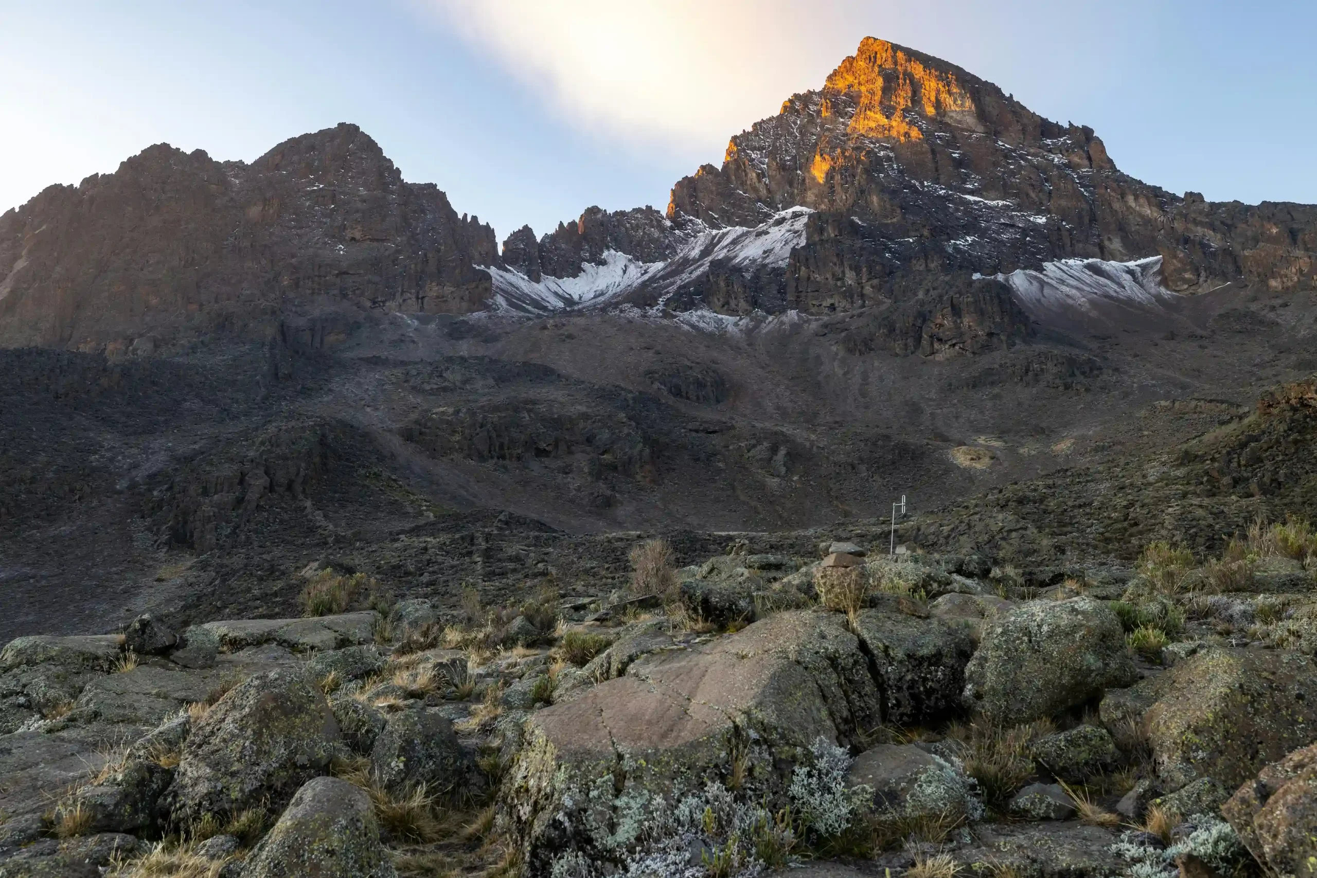 The first light of day on Batian Peak, the highest point of Mount Kenya, with a rugged, rocky landscape below