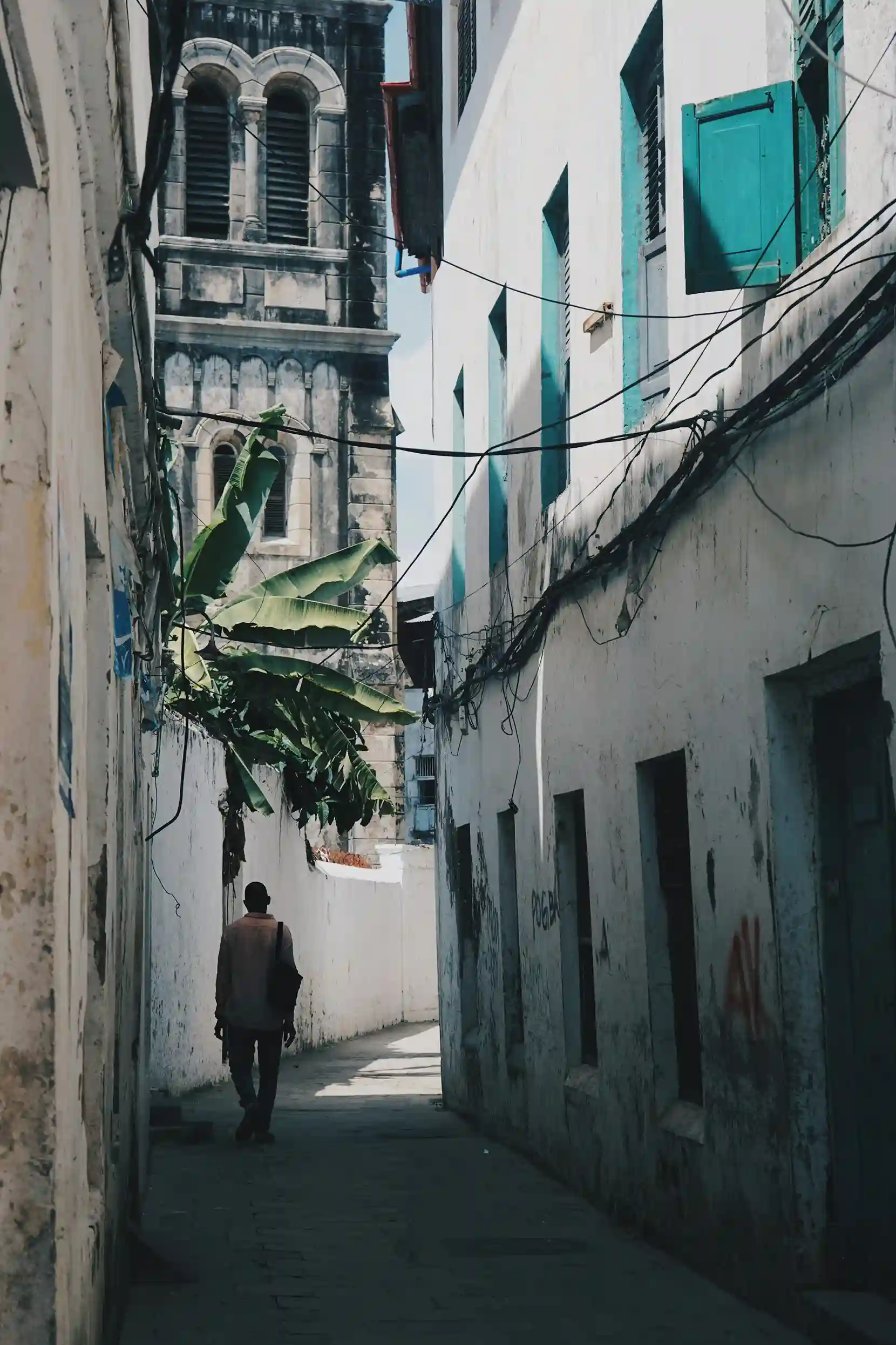 A person walking down a narrow, sunlit alleyway between old buildings in Stone Town, Zanzibar.