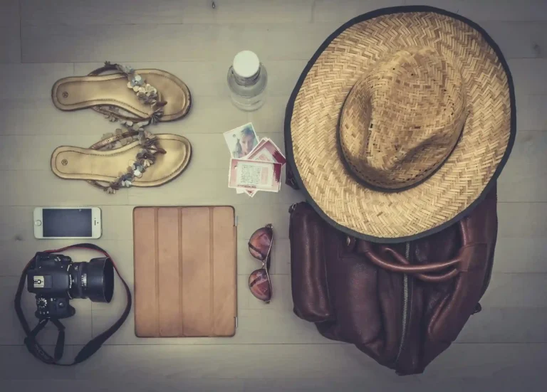 Safari packing flat lay with camera, hat, sandals, sunglasses, and travel accessories.